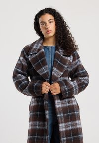Check coat with a brown and blue plaid pattern, oversized collar, and large buttons. Made from a wool-like fabric with a soft texture.