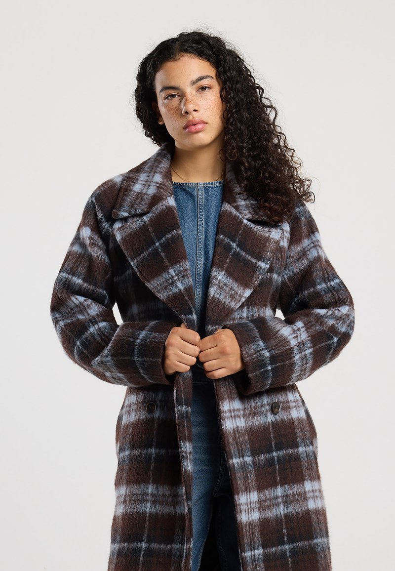 Check coat with a brown and blue plaid pattern, oversized collar, and large buttons. Made from a wool-like fabric with a soft texture.