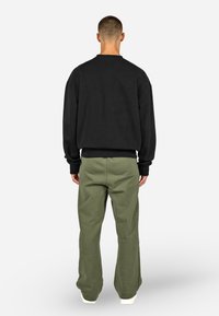 Czarna bluza z okrągłym dekoltem i długimi rękawami, zestawiona z jasnoszarymi spodniami o szerokich nogawkach. Materiał wydaje się miękki, z prążkowanymi ściągaczami.