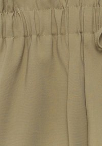 Tissu beige avec détail de taille élastiquée froncée et texture visible de sergé diagonal.