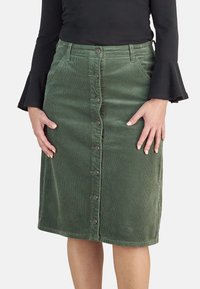 Falda de pana verde con cierre de botones en la parte delantera, cuenta con bolsillos y una silueta recta, tejido texturizado, de longitud a la rodilla.