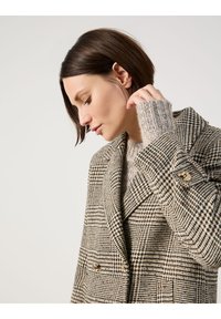 Doppelt gefütterte Blazer im Hahnentrittmuster, in verschiedenen Beige- und Brauntönen, mit goldenen Knöpfen und einem weichen Strickpullover darunter.