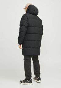 Abrigo de plumas negro con capucha, con secciones acolchadas y un corte holgado. Combinado con pantalones cargo negros y zapatillas.