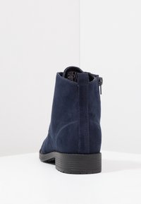 Navy modré semišové kotníkové boty s kulatou špičkou, strukturovaným svrškem, malým černým podpatkem a bočním zipem. Minimalistický design bez ozdob.