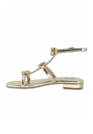 Sandaletto piatto in metallo dorato con sottili cinturini, tre grandi decorazioni con gemme e un piccolo tacco a blocchetto.