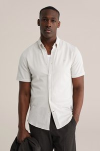 Korte mouwen, lichtbeige overhemd met knopen van zachte stof, met een klassieke kraag en opgerolde mouwen, gedragen met een donkere broek.