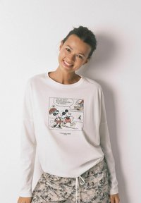 Camicetta bianca a maniche lunghe con stampa a fumetto che presenta Topolino e Minnie. Abbinata a pantaloni da pigiama a fantasia in tonalità tenui.