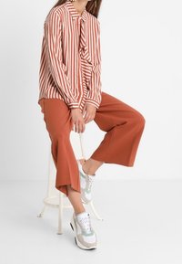 Randig röd och vit skjorta med en slips vid kragen, parat med rostfärgade vida byxor och ljusa sneakers.