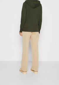 Sudadera con capucha de color verde oliva combinada con pantalones de pierna ancha beiges. Tejido suave con un ajuste relajado, que presenta un bolsillo canguro y puños acanalados.