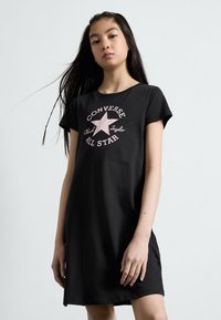 Juoda medvilninė suknelė su trumpomis rankovėmis, su rožiniu žvaigždės grafiku ir užrašu "Converse All Star" krūtinėje.