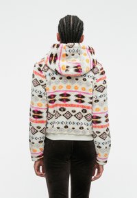 Giacca con cappuccio in pile caratterizzata da motivi geometrici multicolori, prevalentemente in bianco, rosa, arancione e marrone, con un design corto e una texture morbida.