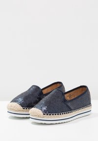 Les espadrilles en sequins navy présentent une semelle en jute et un fond en caoutchouc blanc. Conception à enfiler avec un dessus texturé et un détail de couture contrastant.