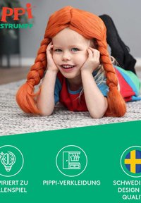 Barnet iført en skarp rød skjorte og et flerfarvet sæt, med langt orange fletet hår, liggende på et struktureret gråt tæppe.