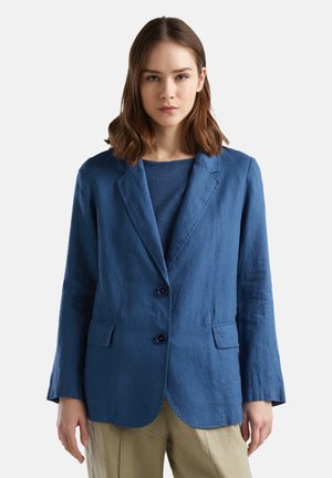 Blazer azul de lino con un diseño ajustado, dos botones, solapas con muesca y dos bolsillos frontales. Lleva una blusa azul texturizada debajo.