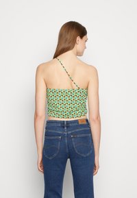 Top cropped em padrões verde e azul com uma alça. O tecido é leve e possui uma textura franzida, combinado com jeans de denim azul.