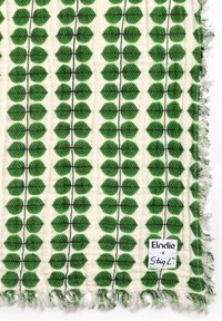 Bomuldsstof med grønne bladmønstre på en cremet baggrund, med frynsekanter og et mærke der viser "Elodie x StigL."