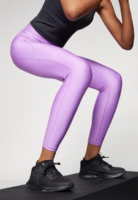 Lila figursydda leggings i stretchmaterial med sid sömmar och en logotyp. Matchas med svarta träning skor på plattform.