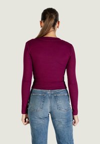 Vínově červený top s dlouhým rukávem spárovaný s světle modrými džínami s vysokým pasem, které mají přiléhavý střih a hladkou, žebrovanou texturu.