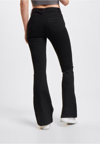 Svarte flared jeans laget av elastisk bomullsblanding, med høy midje, to baklommer og en glatt tekstur.