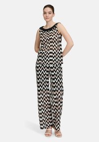 Schwarzer und weißer Zickzackmuster ärmelloser Top kombiniert mit weit geschnittenen Hosen. Der Stoff wirkt leicht und hat eine glatte Textur.