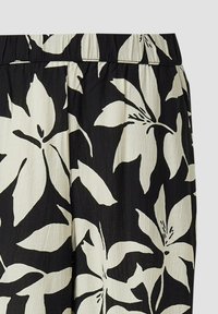 Tissu noir avec de grandes impressions de fleurs de lys tropicales blanc cassé et de subtiles lignes verticales texturées, montrant une partie de la ceinture d'un vêtement.