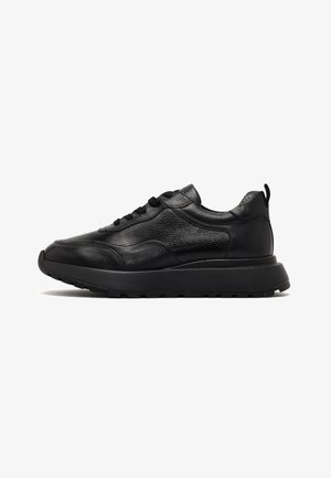 Zwarte leren sneakers met een gestructureerde bovenkant, ronde neus en een dikke rubberen zool. Voorzien van veters en een treklus aan de achterkant.