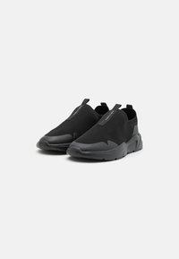 Sneakers neri senza lacci con tomaia in rete, design testurizzato e suola in gomma oversize. Include anche linguette per facilitare l'indossamento.