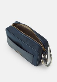 Marineblå crossover taske lavet af nylon, med lynlåslåg, frontlomme, guldfarvet hardware og et mønstret justerbart rem.