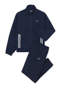 Survêtement bleu marine Lacoste avec veste zippée présentant des détails de fermeture éclair blanche et pantalon à taille élastique assorti, tous deux avec le logo crocodile vert.