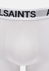 Vita boxershorts med en jämn textur, med ett brett elastiskt midjeband i vitt med svart "ALLSAINTS"-logotyp.