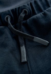 Marineblå joggingbukser har en tekstureret talje med snor. Snorens ender er sorte med prægede 'BAKER' branding. Blødt materiale.