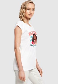 Hvid bomulds t-shirt med et trykt grafik af en pige med teksten "VALIANT" og tropiske elementer. Korte ærmer og et afslappet fit design.