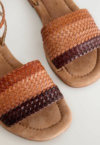 Sandali intrecciati in pelle con tonalità di beige, marrone e marrone scuro. Suole lisce e piatte con una morbida texture in pelle scamosciata e design con punta aperta.