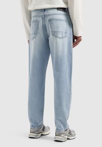 Lichtblauwe denim jeans met een relaxte fit, vijf-pocket ontwerp en minimalistische stiksels. Gecombineerd met grijze sportschoenen.