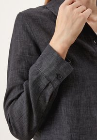 Chemise boutonnée gris foncé avec un tissu texturé, manches longues et un col classique avec un seul bouton au poignet.