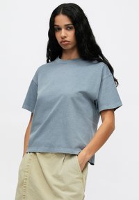 Jasnoniebieski bawełniany t-shirt z krótkim rękawem, lekko luźny krój, okrągły dekolt i surowy brzeg. Noszony z beżową spódnicą.