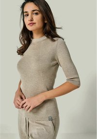 Beiges geripptes Strickoberteil mit kurzen Ärmeln, das über einen Rundhalsausschnitt und eine subtile Struktur verfügt. Das Design beinhaltet ein kleines Logo-Tag am Saum.