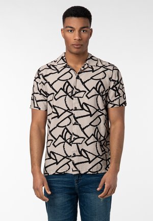 Kurzarmhemd aus beiger Baumwolle mit einem schwarzen abstrakten Muster, klassischem Kragen und vorderer Knopfleiste. Getragen mit blauen Jeans.