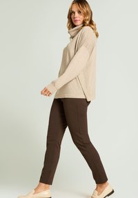 Beige oversized trui met een col, gecombineerd met bruine slim-fit broek en lichtgekleurde loafers, tegen een lichte achtergrond.