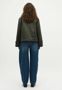 Sötétzöld, rövidített zakó, laza fazonnal, magas derekú, kék, széles szárú farmerral párosítva. A zakón gombos mandzsetta található, és sima tapintású.