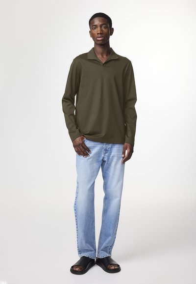 Long-sleeve olive green polo with a collar, paired with light blue straight-leg jeans and black slide sandals, standing against a white background.