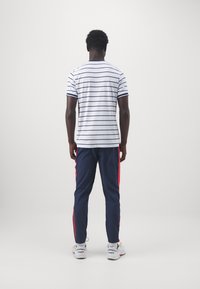 Vit randig t-shirt med korta ärmar, kombinerad med marinblå byxor med röda sidostrickor. Modell med vita och gr å sneakers.