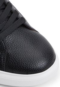 Sneaker in pelle nera con finitura testurizzata, punta rotonda e suola in gomma bianca. Presenta lacci neri e una linguetta liscia.