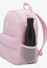 Ροζ σακίδιο με λευκές λεπτομέρειες, που διαθέτει πλαϊνή τσέπη από δίχτυ με ένα μαύρο παγούρι νερού. Κατασκευασμένο από ανθεκτικό ύφασμα με στρογγυλεμένο σχήμα.