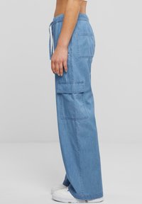 Světle modré džíny cargo s volným střihem, vybavené elastickým pasem, stahovací šňůrkou a dvěma bočními kapsami. Texturovaná látka, široké nohavice.