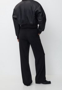 Schwarze, kurz geschnittene Bomberjacke aus Leder mit übergroßen Ärmeln, kombiniert mit hoch taillierten, schwarzen Hosen mit weitem Bein. Glatte Textur und minimale Details.