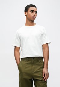 Λευκό βαμβακερό μπλουζάκι με κοντά μανίκια, συνδυασμένο με πράσινο παντελόνι ίσιας γραμμής. Το παντελόνι διαθέτει κουμπί κλεισίματος και τσέπες.