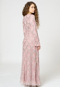 Langes pinkes Abendkleid mit figurbetonter Silhouette, geschmückt mit silbernen, paillettenbesetzten geometrischen Mustern und langen Ärmeln. Glattes, strukturiertes Material.