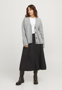 Cardigan en maille gris clair avec des boutons, associé à un t-shirt blanc et une jupe maxi noire. Des bottes noires jusqu'aux genoux complètent la tenue.