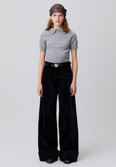 Top de punto gris de manga corta con un cuello texturizado, combinado con pantalones de correa negros de pierna ancha con pliegues frontales y una hebilla dorada.